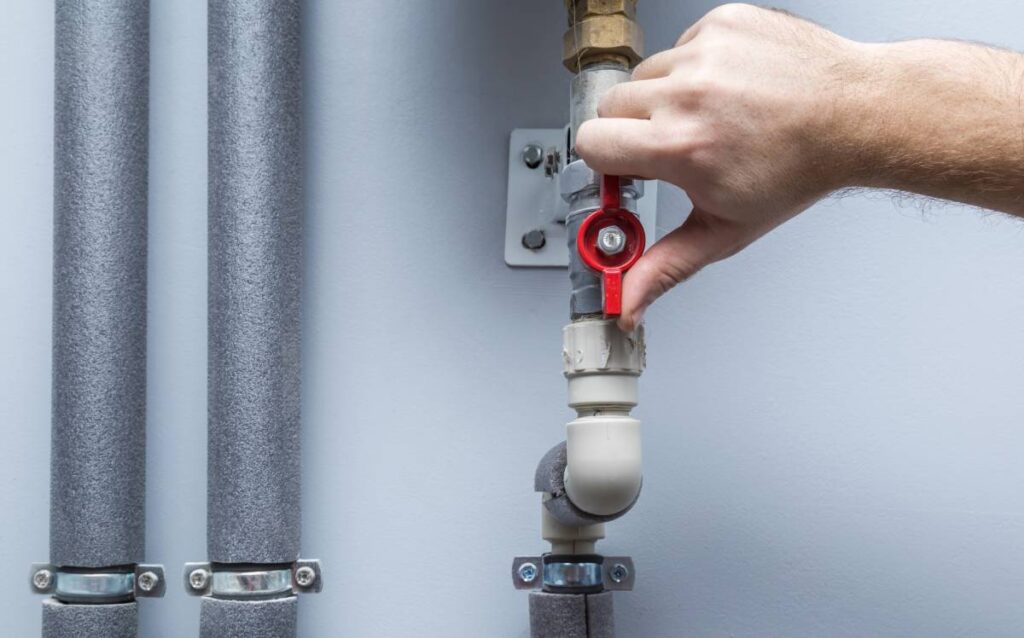 Mano girando la manivela roja de una llave de paso de agua metálica en una pared