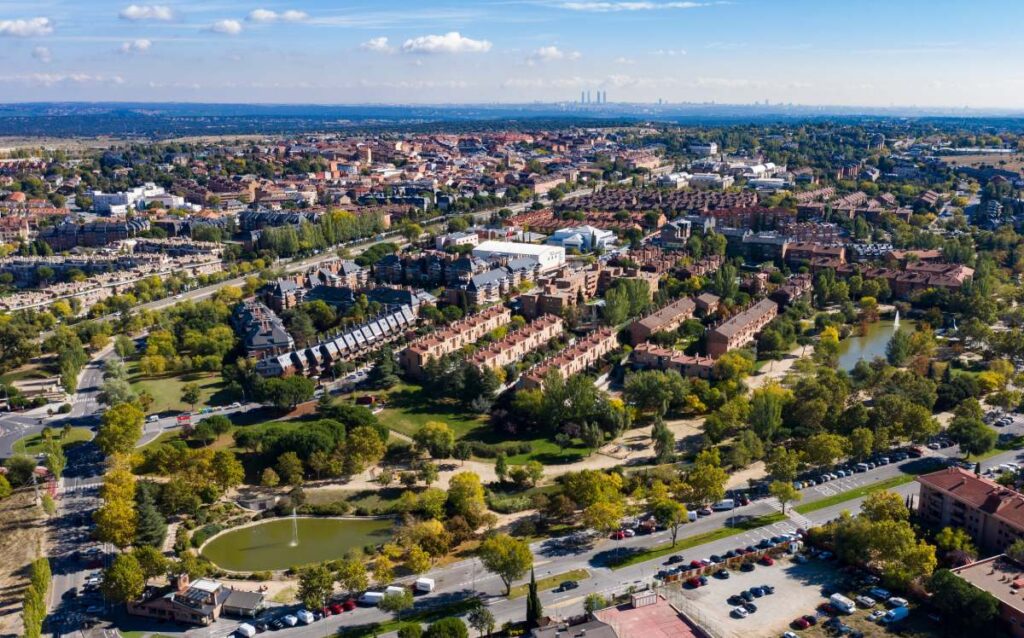 Vista aérea de un municipio residencial en las afueras de Madrid, con abundantes zonas verdes y un lago en primer plano