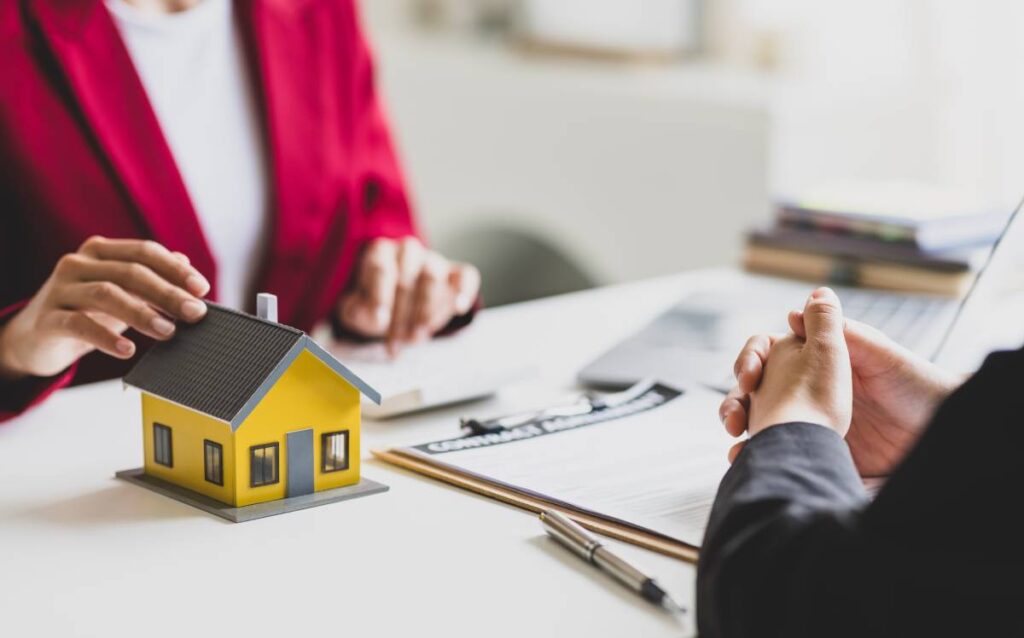 Maqueta de casa amarilla sobre una mesa durante una firma de contrato
