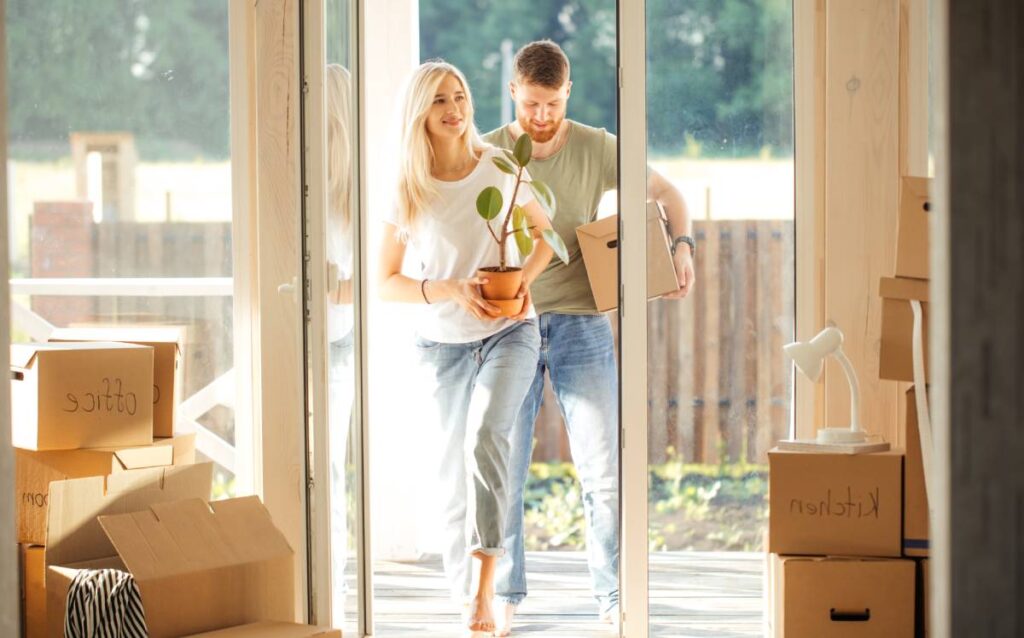 Pareja entrando a su nueva casa con cajas y una planta, simbolizando el comienzo de una mudanza organizada