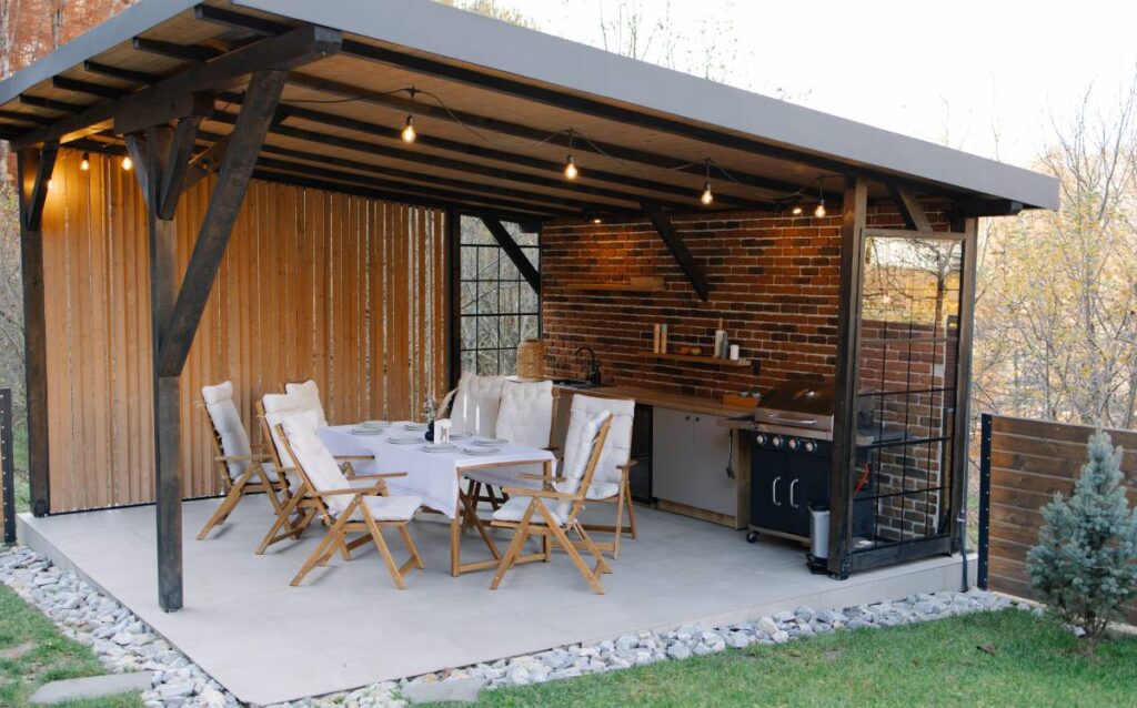 Cocina exterior integrada y comedor bajo una pérgola de madera en una terraza grande