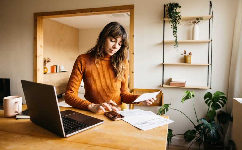 Mujer revisando facturas y gestionando los gastos fijos del hogar con un ordenador y calculadora