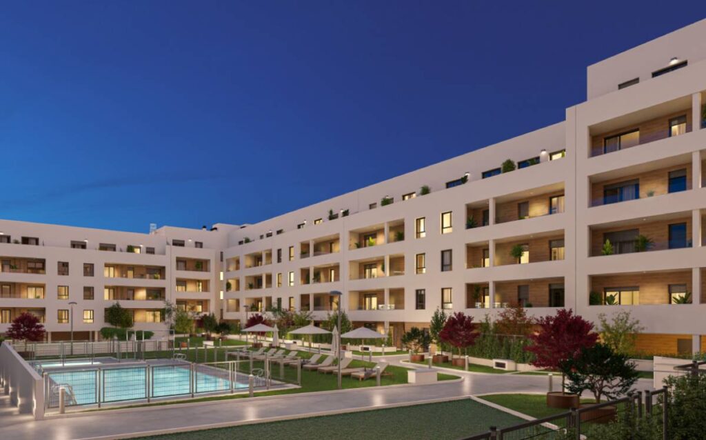 Fachada moderna del edificio residencial Célere Morelia en Valladolid con piscina iluminada y zonas comunes por la noche