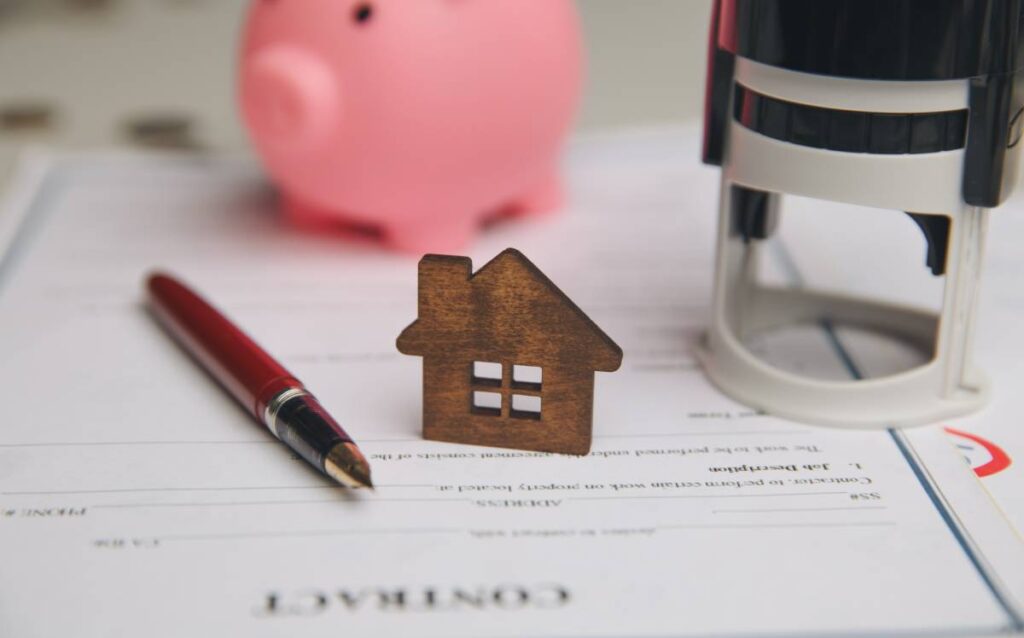 Gastos notariales compra vivienda: contrato, miniatura de casa y hucha