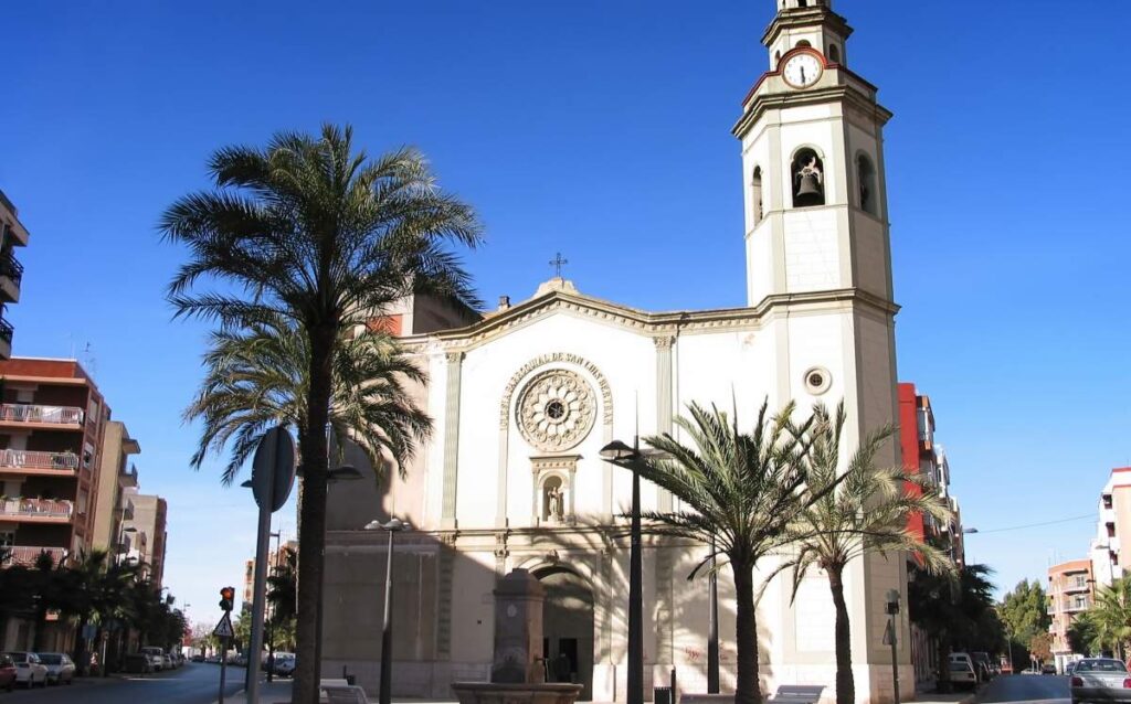 Fachada de la Iglesia Parroquial de San Luis Bertrán en Torrent, con su torre campanario y palmeras bajo un cielo despejado