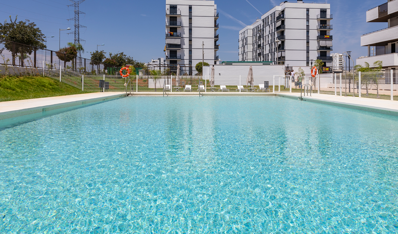 Área de piscina comunitaria de Célere Arce integrada en un entorno residencial moderno, con zonas verdes, espacios de ocio exterior y edificios de diseño contemporáneo al fondo.