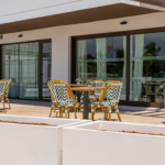 Terraza comunitaria de Célere Arce con mesas y sillas al aire libre, amplios ventanales y acceso a las zonas comunes interiores.