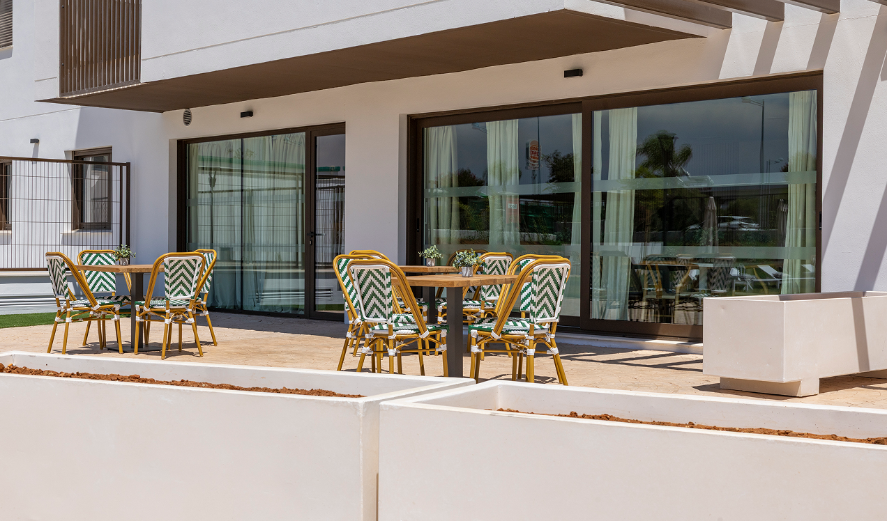 Terraza comunitaria de Célere Arce con mesas y sillas al aire libre, amplios ventanales y acceso a las zonas comunes interiores.