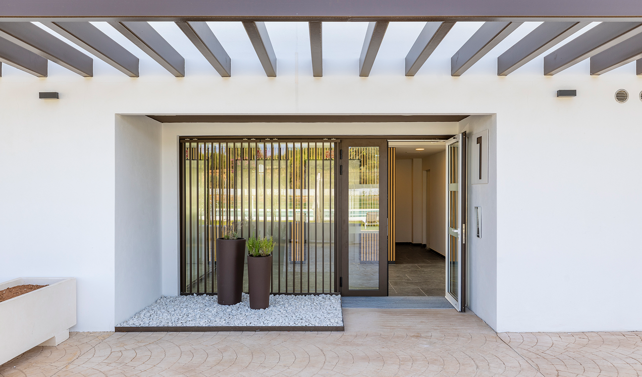 Entrada principal de Célere Arce con acceso al edificio residencial, diseño contemporáneo, acabados modernos, zonas ajardinadas decorativas y espacios comunes acondicionados.