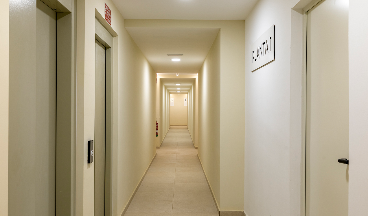 Pasillo interior de Célere Arce con acceso a viviendas, ascensores, iluminación moderna y zonas comunes.