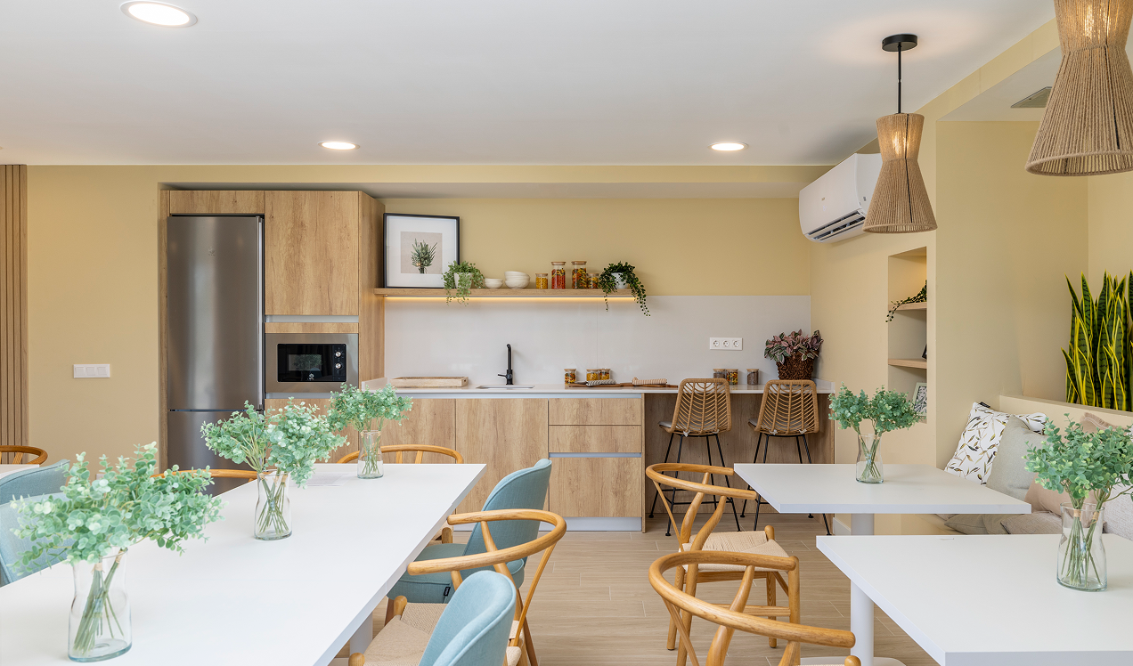 Sala social de Célere Arce con cocina equipada, mesas para reuniones, zona de comedor y espacios comunes diseñados para el ocio, la convivencia y el disfrute de los residentes.