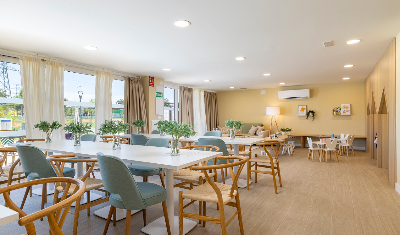 Sala comunitaria de Célere Arce con mesas, sillas, zona de descanso, espacio infantil y amplios ventanales en un entorno moderno y multifuncional.