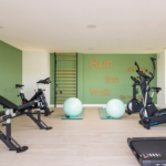 Gimnasio comunitario de Célere Arce con máquinas de cardio, banco de musculación, bicicletas estáticas, zona de entrenamiento funcional y espejos grandes.