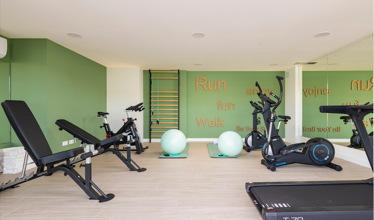 Gimnasio comunitario de Célere Arce con máquinas de cardio, banco de musculación, bicicletas estáticas, zona de entrenamiento funcional y espejos grandes.