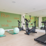 Gimnasio comunitario de Célere Arce equipado con cintas de correr, bicicletas estáticas, zona de entrenamiento funcional, espejos de gran formato y espacio para ejercicios de bienestar.
