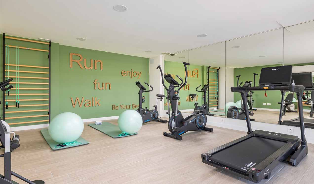 Gimnasio comunitario de Célere Arce equipado con cintas de correr, bicicletas estáticas, zona de entrenamiento funcional, espejos de gran formato y espacio para ejercicios de bienestar.