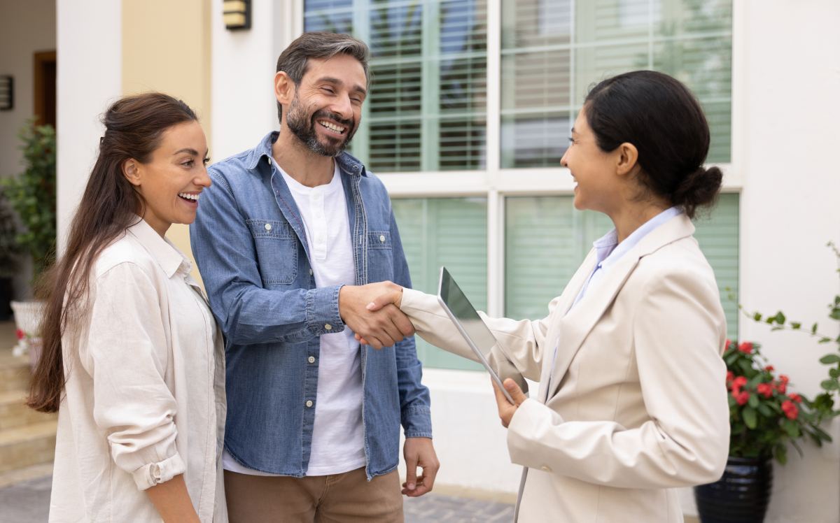 Pareja sonriente dando la mano a agente inmobiliario que sostiene una tableta