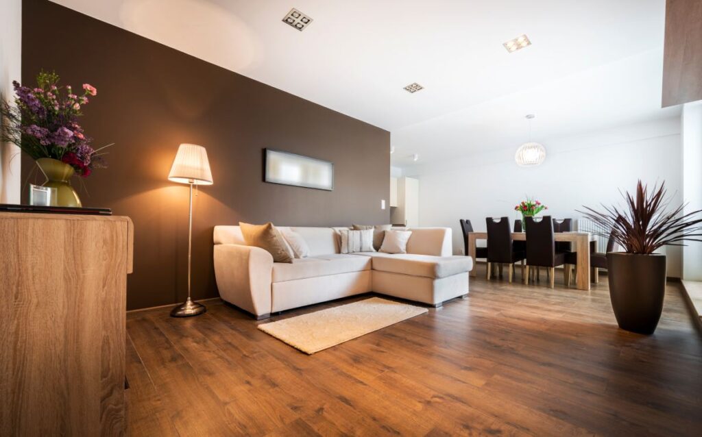 Salón moderno con pared marrón, sofá beige y zona de comedor al fondo