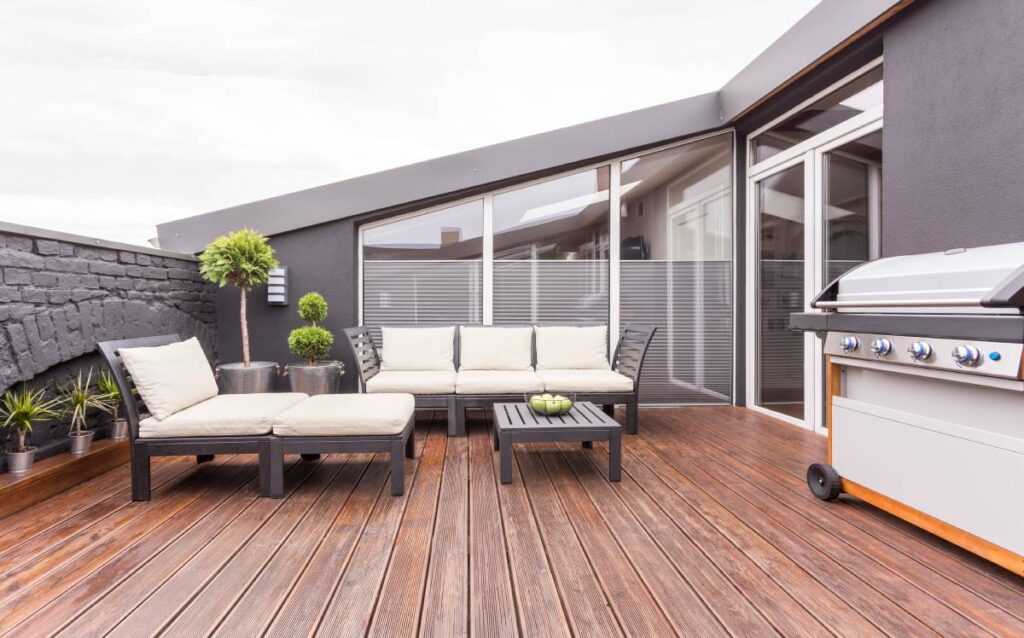 Terraza de un ático con suelo de tarima de madera, sofás de exterior modernos, plantas decorativas y una barbacoa de gas