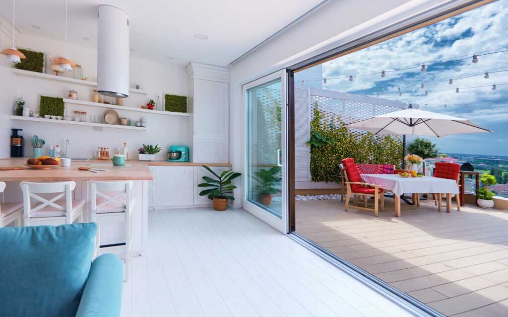 Cocina moderna y luminosa abierta a una amplia terraza con comedor exterior bajo una sombrilla y vistas despejadas