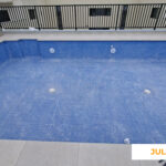 La imagen muestra el avance de las zonas comunes de Célere Arts II en julio de 2026, con una piscina exterior en fase final de ejecución, revestimiento cerámico azul instalado, sistemas de impulsión y desagüe visibles.