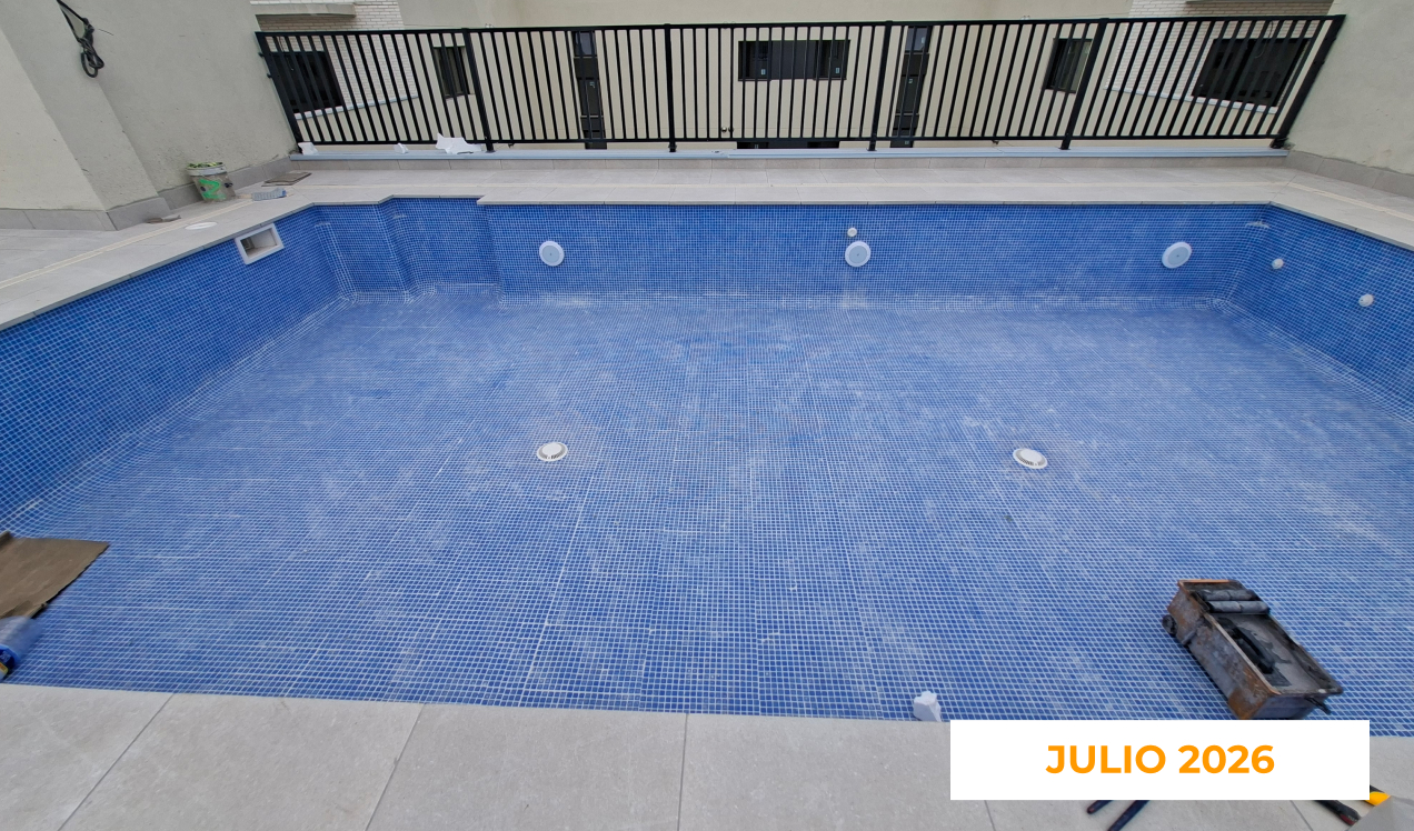 La imagen muestra el avance de las zonas comunes de Célere Arts II en julio de 2026, con una piscina exterior en fase final de ejecución, revestimiento cerámico azul instalado, sistemas de impulsión y desagüe visibles.