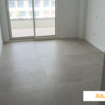 La imagen muestra el interior de una vivienda de Célere Opal en julio de 2026, con acabados prácticamente finalizados, suelo porcelánico de gran formato, paredes pintadas en blanco y acceso a una amplia terraza a través de una puerta corredera acristalada.