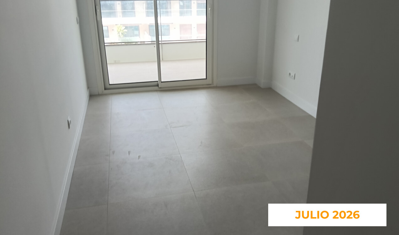 La imagen muestra el interior de una vivienda de Célere Opal en julio de 2026, con acabados prácticamente finalizados, suelo porcelánico de gran formato, paredes pintadas en blanco y acceso a una amplia terraza a través de una puerta corredera acristalada.