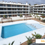 La imagen muestra las zonas comunes de Célere Opal en julio de 2026, con una piscina exterior, área de spa o piscina de hidroterapia, espacios ajardinados con vegetación mediterránea y edificios residenciales prácticamente terminados.