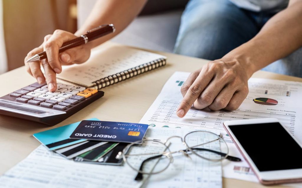 Persona revisando gastos del hogar con calculadora, facturas y tarjetas bancarias