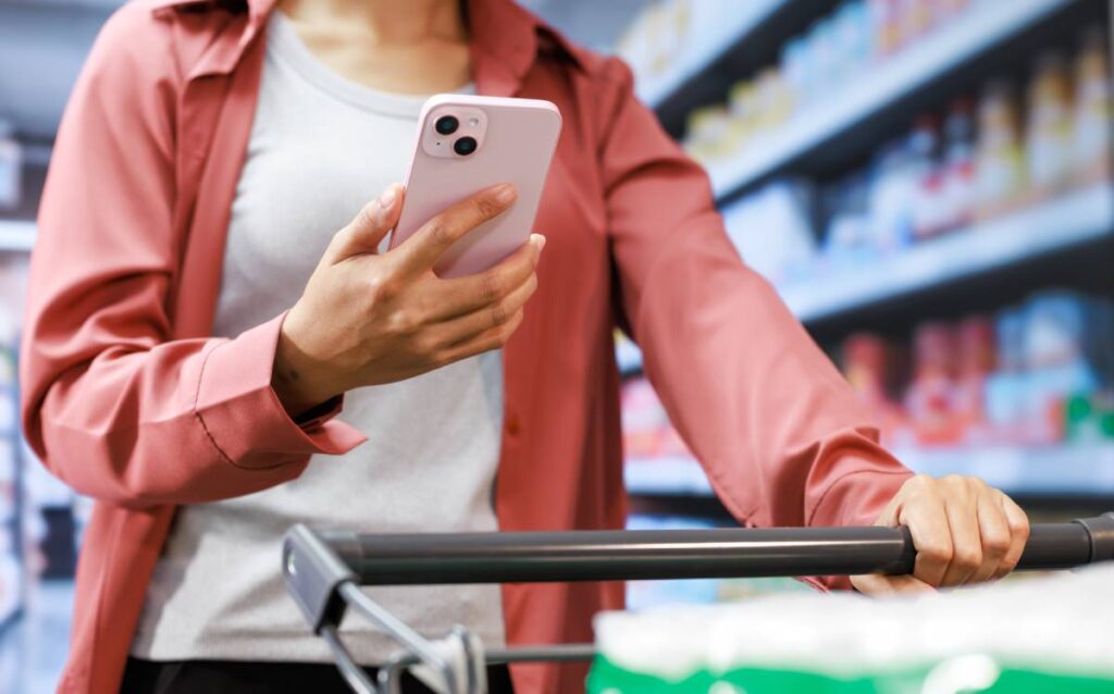 Mujer consultando el móvil mientras realiza la compra en un supermercado