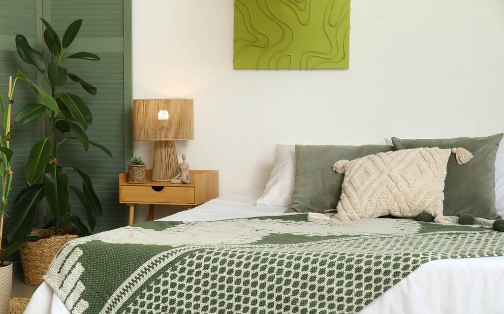 Dormitorio decorado en tonos blancos y verdes con textiles estampados, cojines y muebles de madera natural