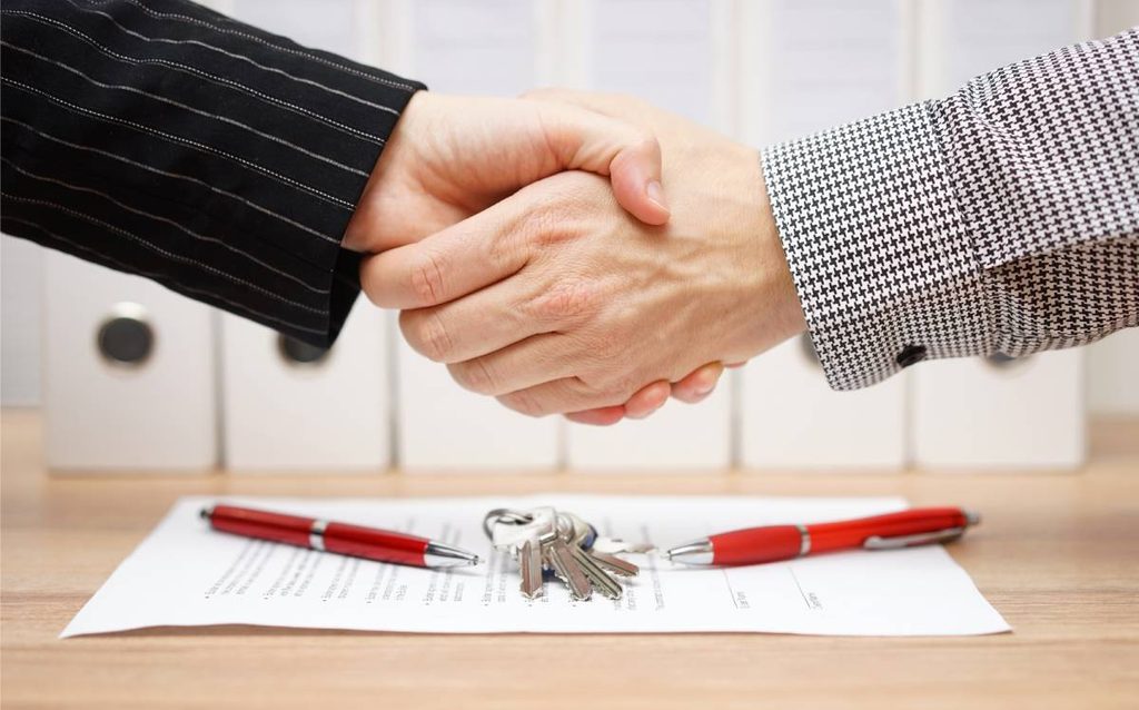 Apretón de manos tras un acuerdo hipotecario, con contrato de compraventa y llaves de una vivienda sobre la mesa