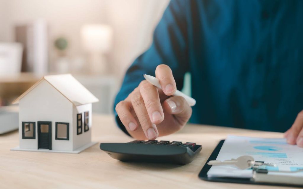 Persona calculando el presupuesto para comprar una casa con una calculadora y una maqueta de vivienda