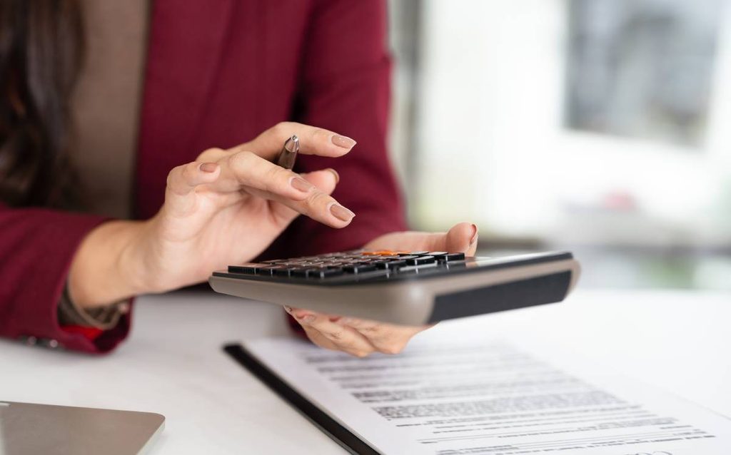 Mujer utilizando una calculadora para revisar sus gastos y ahorros antes de comprar una vivienda