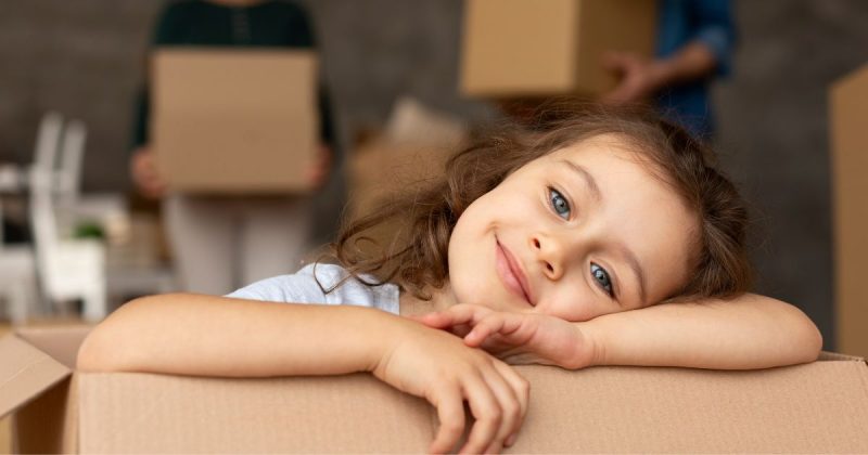 Niña sonriendo apoyada sobre una caja de cartón de una mudanza